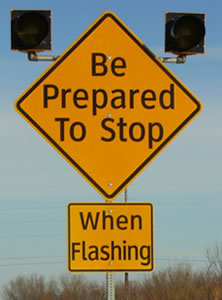 Diamond-shaped warning sign with the legend "Be Prepared To Stop" with a rectangular plaque below with the legend "When Flashing." Both legends are displayed in upper- and lower-case letters of the alternative alphabet.