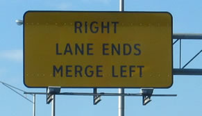 Center right is a rectangular warning sign that displays the legend "RIGHT LANE ENDS MERGE LEFT" in the alternative alphabet in a negative-contrast orientation.