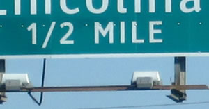 A guide sign distance legend of "½ MILE" is shown. The numerals and solidus of the fraction are aligned as a single line instead of the numerals being arranged diagonally about the solidus.
