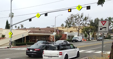 This photo shows an uncontrolled marked crosswalk.  A Yield Here To Pedestrians (R1-5a) sign is post-mounted prior to the crosswalk on the right-hand side of the roadway.  A mast arm extends in a cantilever fashion over the crosswalk from a support pole on the left-hand side of the roadway adjacent to the crosswalk.  A Pedestrian (W11-2) warning sign with a diagonal downward pointing arrow (W16-7P) plaque is mounted on the mast arm support pole.  Two single-section warning beacons are mounted on the mast arm for each direction of travel and only one of the yellow indications facing the camera is illuminated, which means that they are flashing in an alternating manner.  Two Pedestrian (W11-2) warning signs are mounted on the mast arm, one of which is between the two warning beacons facing the opposing direction of travel and one of which is between the two warning beacons facing the camera.