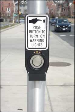 Figure 3 shows a pedestrian pushbutton detector mounted on a pole.  Above the detector are three illuminated small yellow lights that indicate to the pedestrian that the button press has been received by the controller.  Above the pilot lights is a Push Button to Turn On Warning Lights (W10-25) sign.