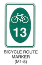 Pedestrian and Bicycle Sign "BICYCLE ROUTE MARKER (M1-8)" is shown as a vertical rectangular white sign. It shows a green oval with a white symbol of a bicycle above the white numerals "13" on the oval.