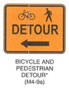 Pedestrian and Bicycle Sign "BICYCLE AND PEDESTRIAN DETOUR (M4-9a)" is shown as an orange sign with a black border and legend. It shows symbols for a left-facing bicycle and left-facing walking person on the top line, the word "DETOUR" on the middle line, and a horizontal left-pointing arrow on the bottom line. This sign was anticipated for inclusion in the 2003 edition of the MUTCD at the time of this printing.