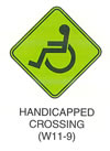 Pedestrian and Bicycle Sign "HANDICAPPED CROSSING (W11-9)" is shown as a green with black borders and legends, diamond-shaped symbol sign with a stylized symbol of a left-facing person in a wheelchair.