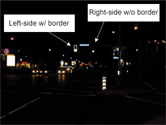 photo depicting two signal heads at a distant intersection at night, one with reflective border and clearly visible, one without border and lost amidst other lights.