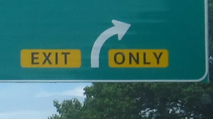 The photograph at center left is a rectangular warning panel within a guide sign that displays the legend "EXIT ONLY" in the alternative alphabet in a negative-contrast orientation.