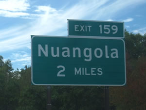 An image of a guide sign is shown with the legend "Nuangola 2 MILES." The destination of Nuangola is displayed in upper- and lower-case letters of the alternative alphabet. The distance legend of 2 MILES is shown in all upper-case letters of the Standard Alphabets.
