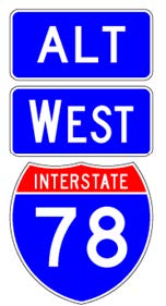 A sign assembly comprised of a full color Interstate route shield sign above which is a white-on-blue cardinal direction auxiliary sign above which is a white-on-blue "Alt" auxiliary sign.