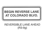 Regulatory Sign "REVERIBLE LANE AHEAD (R3-9g)" is shown as a horizontal rectangular white sign with a black border and legend. The words "BEGIN REVERSE LANE AT COLORADO BLVD." in black are shown on two lines.