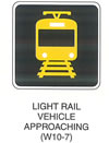 Railroad and Light Rail Transit Grade Crossing Sign "LIGHT RAIL VEHICLE APPROACHING (W10-7)" is shown as a square black sign with a yellow border and legend. It shows a yellow symbol of a head-on view of a light rail transit vehicle on a track.