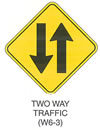 Warning Sign "TWO WAY TRAFFIC (W6-3)" is shown as a diamond-shaped sign. It shows a vertical downward-pointing arrow to the left of a vertical upward-pointing arrow.